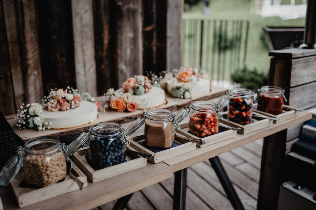 Torten mit Blumen und bunten Fruchtgläsern auf rustikalem Holztisch in Dienten.