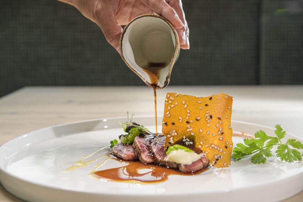 Saftiges Fleischgericht mit Sauce, Garnitur und knuspriger Beilage auf weißem Teller.