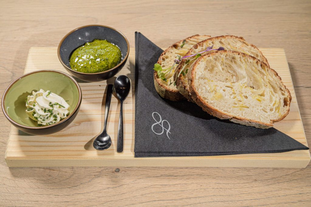 Frisches Brot mit Kräuterbutter und Pesto auf einem Holzbrett serviert.