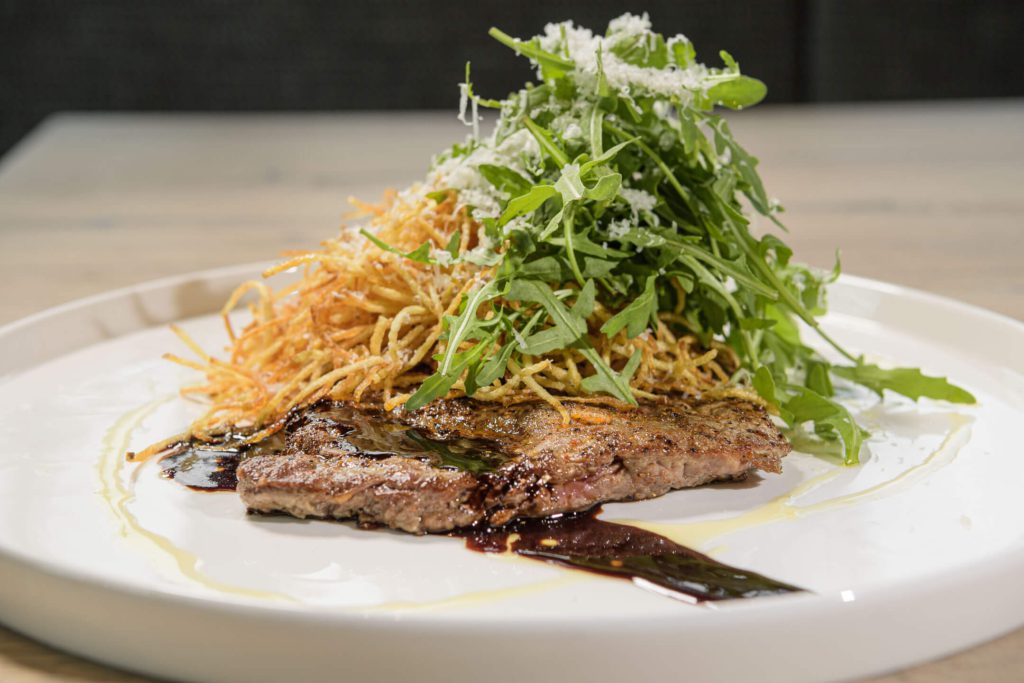 Saftiges Steak mit Rucola und knusprigen Kartoffelstreifen auf einem Teller angerichtet.