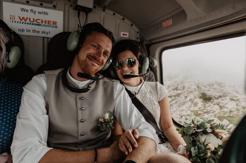 Brautpaar mit Headsets im Helikopter vor alpiner Berglandschaft Hochkönig