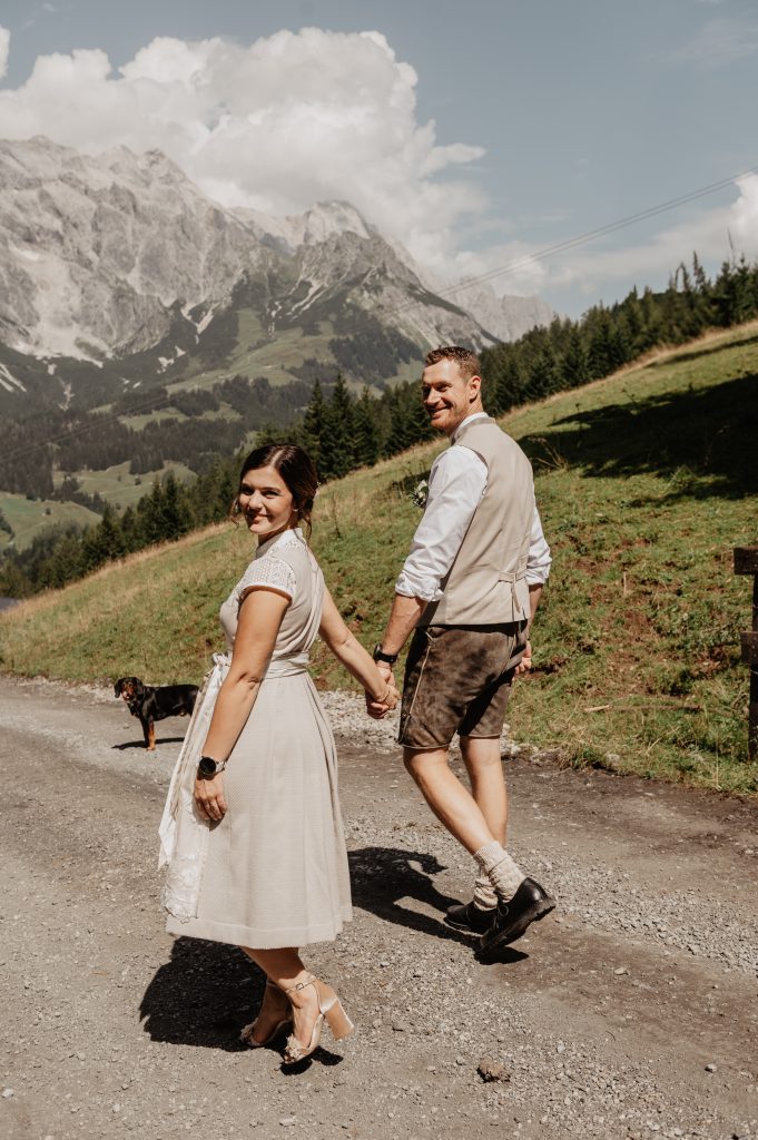 Paar in Tracht spaziert Hand in Hand vor Alpenpanorama bei Dienten am Hochkönig