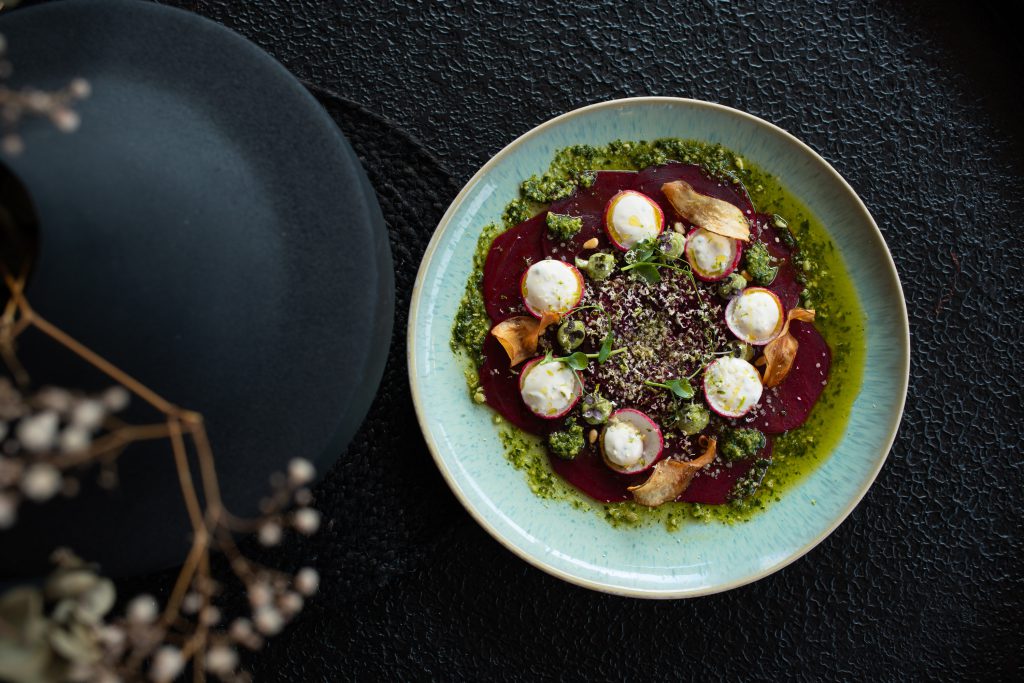 Carpaccio mit Ziegenkäse und Kräutern auf grünem Pesto angerichtet